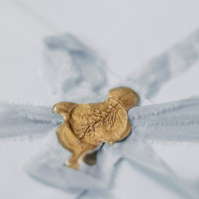 Hochzeitspapeterie: Goldener Wachssiegel auf Seidenband gießen, hellblauer Briefumschlagm Siegelstempel