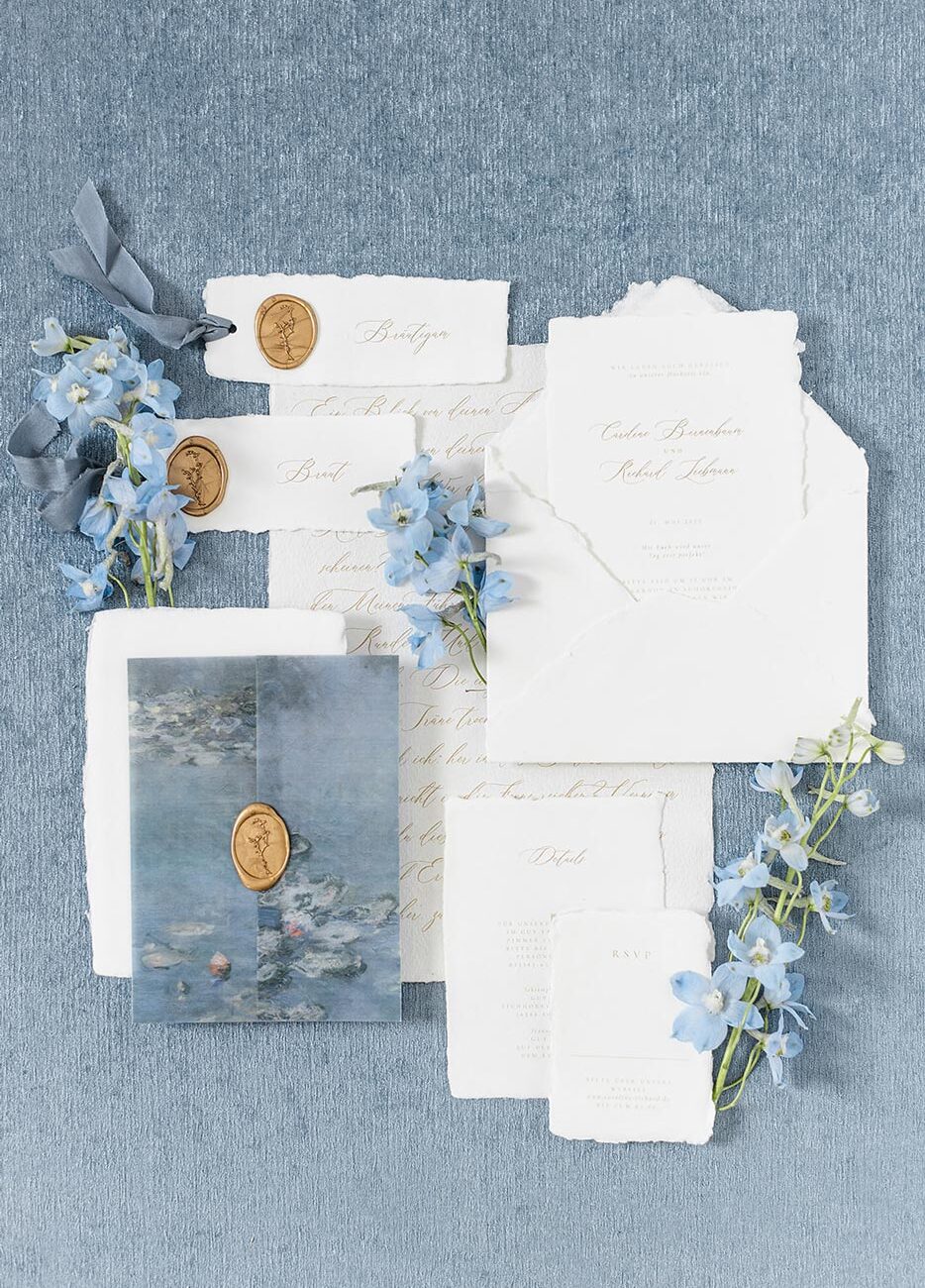 Elegante Hochzeitseinladung für eine Fine Art Hochzeit in weiß und hellblau mit moderner Kalligrafie handgeschöpften Papier und blauen Einschlagpapier aus Transparentpapier. Veredelt mit goldenen Wachssiegeln