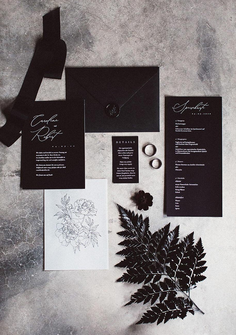 Individuelle Hochzeitseinladung in Schwarz mit schwarzen Wachssiegel und Rosen Skizze auf Transparentpapier im Flatlay