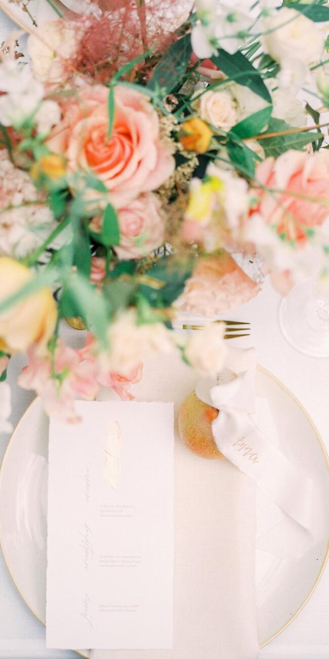 Elegante Menükarte mit Gold veredelung und kalligrafie liegt auf einem Hochzeitstisch mit Blumenstrauß und goldenen Besteck