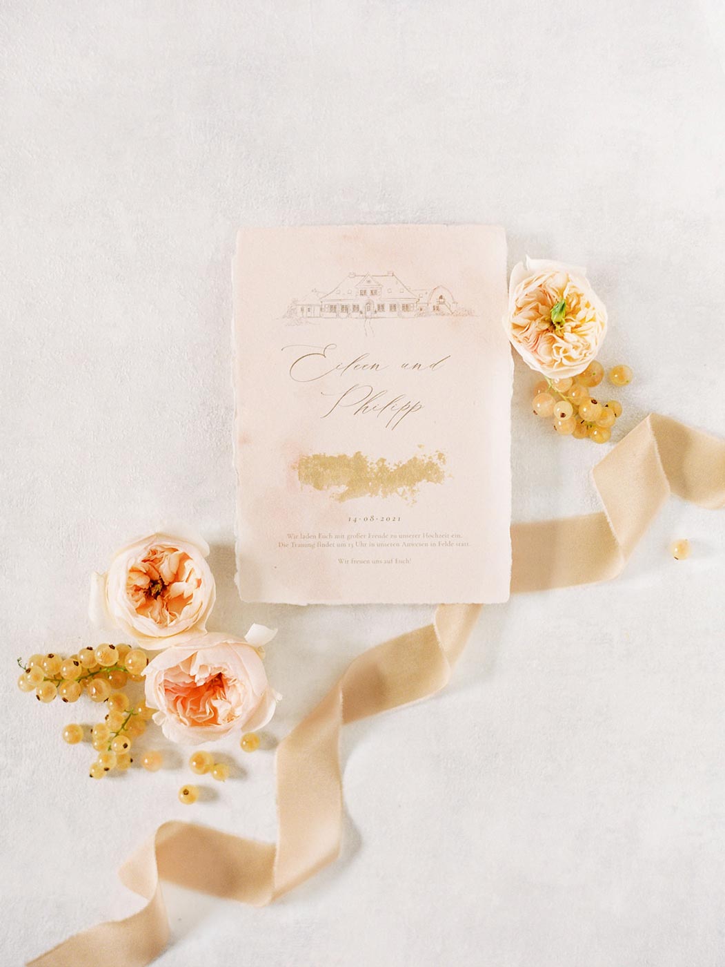 Individuelle Hochzeitseinladung in einem Flatlay für eine Fine Art Hochzeit aus handgeschöpften Papier mit einer Hochzeitslocation Zeichnung mit Goldveredelung