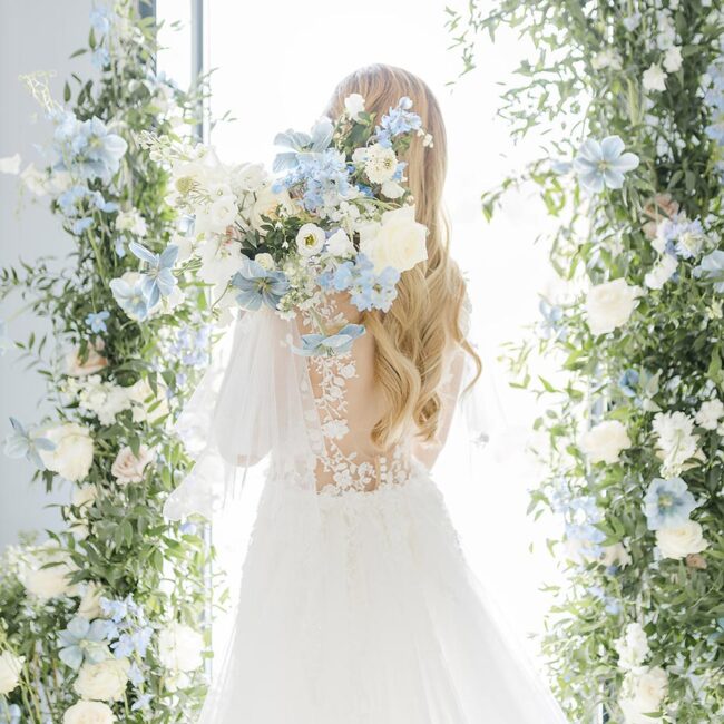 Fine Art Hochzeitsfotografie von einer Braut in einem Hochzeitskleid vor Blumenarrangement mit einem Blumenstrauß