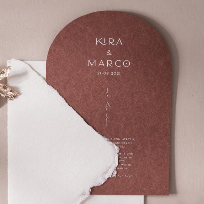 Hochzeitseinladung aus Terrakotta farbenen Papier in Torform, weiß bedruckt mit einem handgeschöpften Briefumschlag