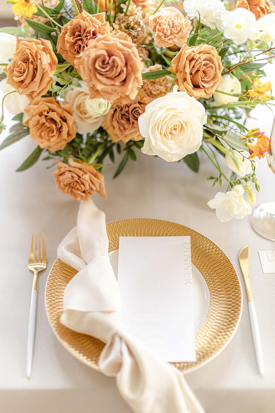 Moderne Menükarte liegt auf einem dekorierten Hochzeitstisch mit goldenem Teller und Besteck mit orangenen und weißen Rosen