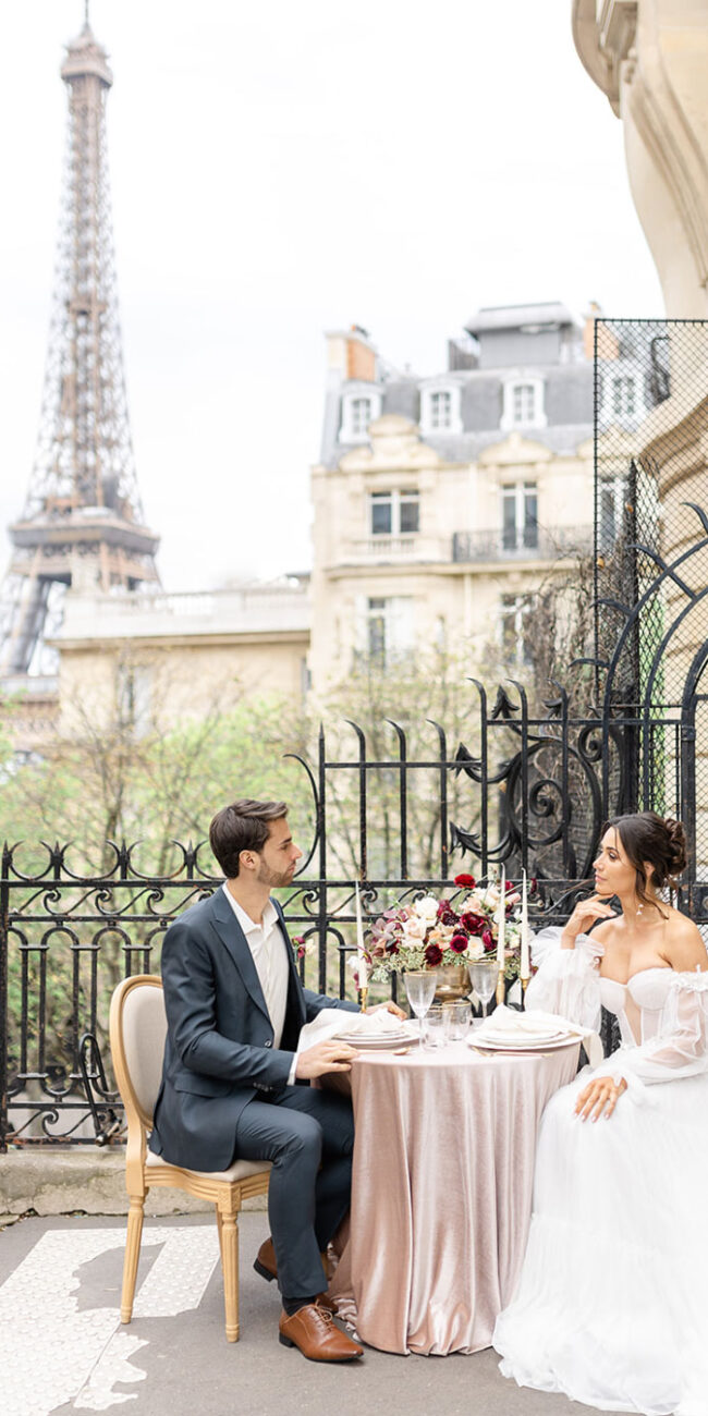 Lachendes Brautpaar beim Dinner in Paris. Die Braut trägt ein Hochzeitskleid mit Hochzeit Blumenstrauß in Dunkelrot, Rose und Weiß. Hochzeitsdekoration und Blumen