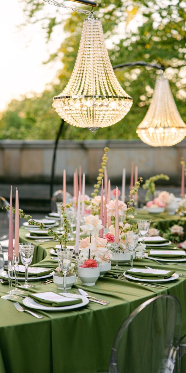 Hochzeitstafel mit grüner Tischdecke, weißen und rosa Blumen und Kronleuchtern
