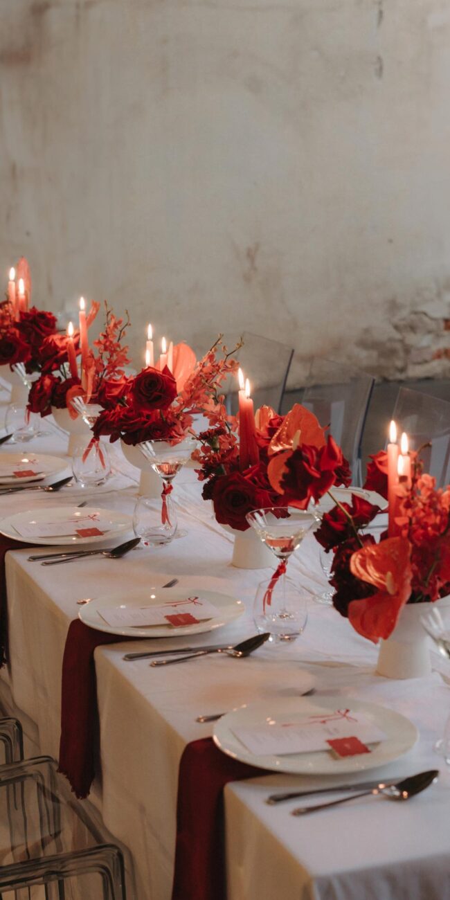 Elegant gedeckte Hochzeitstafel mit roten Blumen, weißen Tischdecken und Kerzen