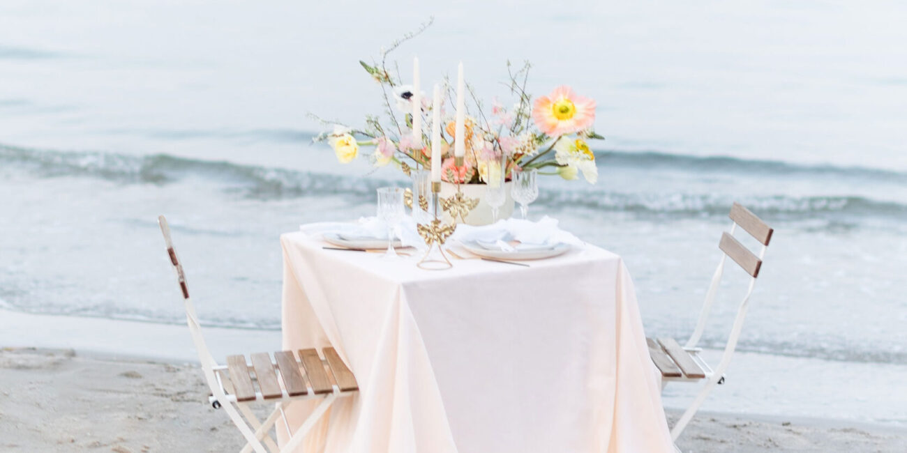 Hochzeitstisch am Strand mit floraler Tischdekoration in Peach, Apricot, Rosa und Weiß