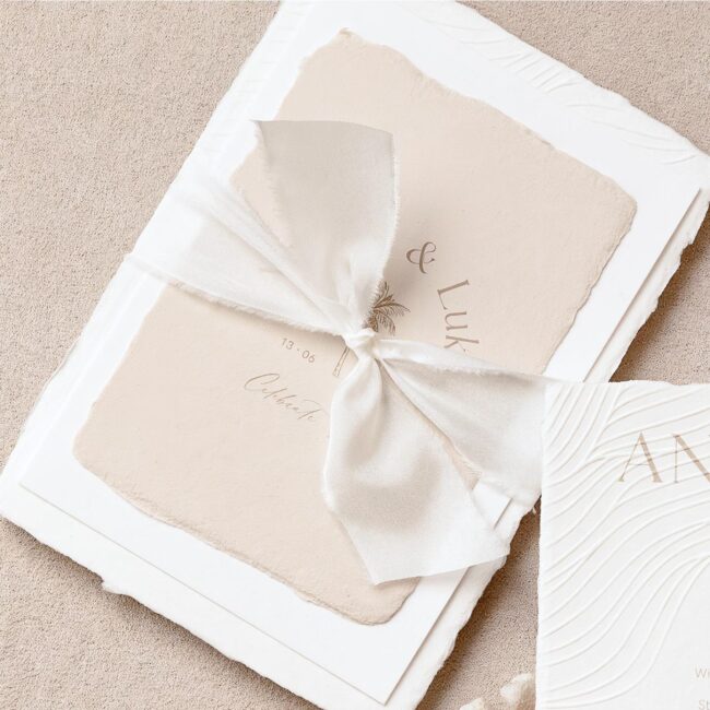 Individuelles Hochzeitseinladungsset aus handgeschöpftem Papier in Beige mit einem weißen Seidenband für eine Strandhochzeit in einem Beach Club auf Ibiza