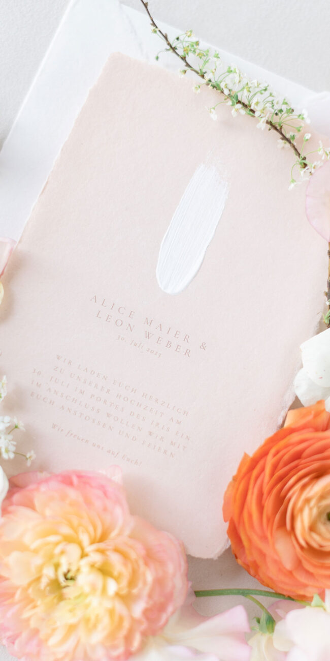 Detailaufnahme einer handgeschöpften Hochzeitseinladung mit weißem Pinselstrich, feiner Typografie und zartem Peachton