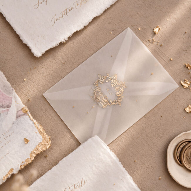 Individuelles Hochzeitslogo in gold per Heißfolienprägung veredelter Kranz auf einem transparenten Umschlag