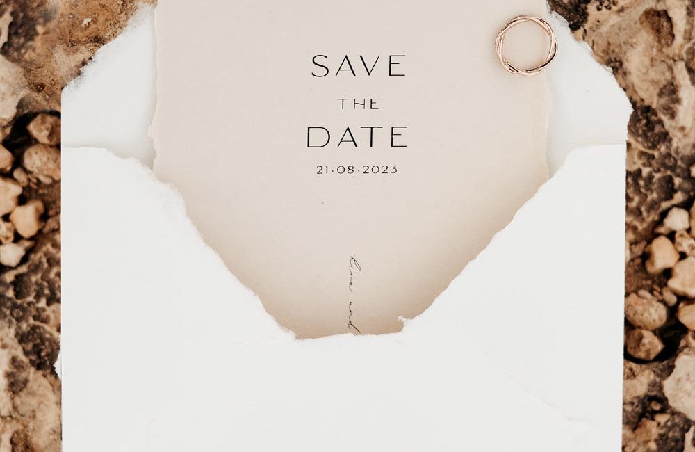 Hochzeitspapeterie Strandhochzeit: Moderne Save The Date Karte in Weiß und Sand aus handgeschöpften Papier, Flatlay auf Sandstein